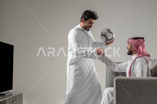الشغف في متابعة فريق كرة القدم، قضاء وقت الفراغ بمشاهدة التلفاز مع الأصدقاء، الانتصار و تحقيق الأهداف، بورتريه مقرب لرجلان عربيان سعوديان يحتفلان بفوز فريقهم المفضل، ايماءات الحماس والسعادة والسرور، خلفية رمادية