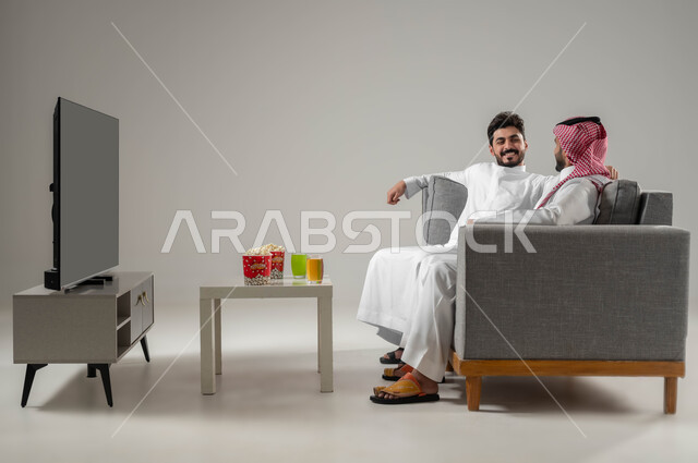 الاستمتاع بتبادل الاحاديث بين الصديقين, تعابير التسلية والمرح, بورتريه لرجلان عربيان سعوديان خليجيان, نشاط منزلي ترفيهي جماعي, قضاء اوقات ممتعة ومسلية مع الاصدقاء, مفهوم العلاقة لقوية والترابط بين الزملاء, خلفية رمادية