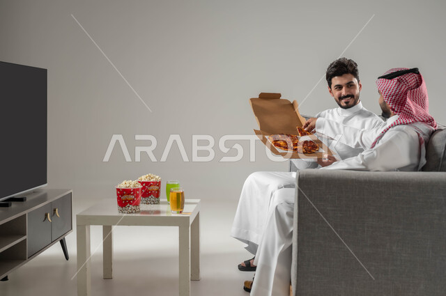 Eating pizza and snacks, spending enjoyable times with friends, portrait of two Saudi Gulf Arab men, recreational activities in free time, the concept of strong relationships and interconnectedness between colleagues, gray background