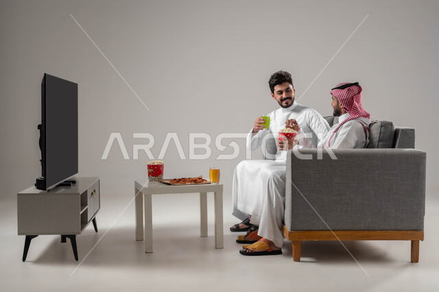 الاستمتاع باوقات الفراغ, نشاط منزلي ترفيهي جماعي, المتعة في تناول الفشار اثناء مشاهدة التلفاز. قضاء اوقات ممتعة بين الاصدقاء, بورتريه لرجلان عربيان سعوديان خليجيان, مشاهدة الافلام والعروض المسرحية, خلفية رمادية