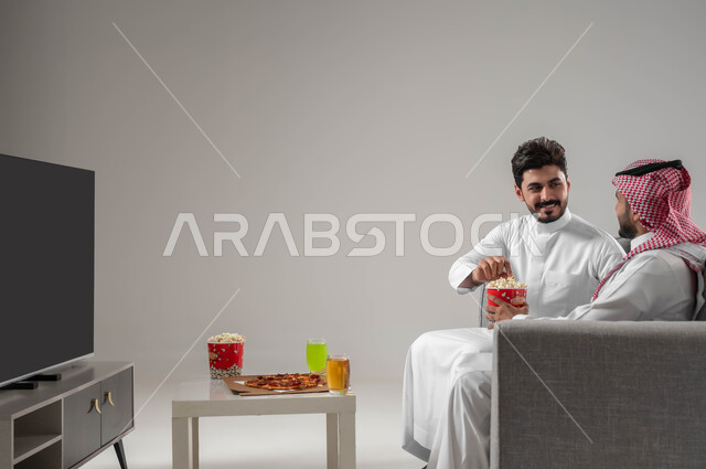 الاستمتاع بتناول الفشار اثناء مشاهدة التلفاز. قضاء اوقات ممتعة بين الاصدقاء, بورتريه لرجلان عربيان سعوديان خليجيان, مشاهدة الافلام والعروض المسرحية, نشاط منزلي ترفيهي جماعي, خلفية رمادية