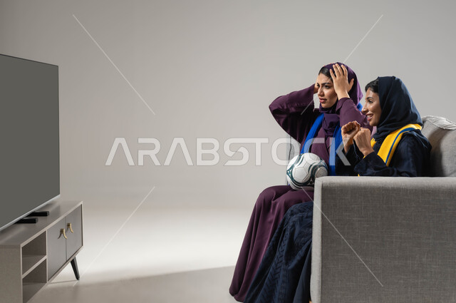 رفع اليدين بإيماءات الفوز والانتصار، تعابير الحزن لخسارة الفريق، ارتداء اوشحة تشجيعية، بورتريه لشابتان عربيتان خليجيتان سعوديتان تجلسان على كنبة مريحة تحمل إحداهما كره، متابعة المباريات والالعاب الرياضية، مشاهدة التلفاز مع العائلة، خلفية رمادية