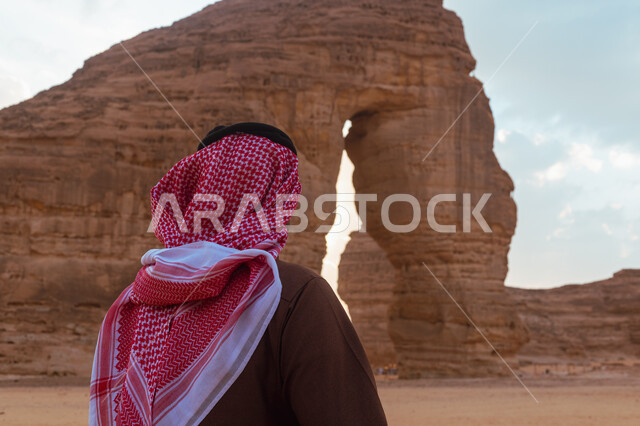 صخرة الفيل في محافظة العلا في السعودية، معالم اثرية تاريخية قديمة في وقت النهار، التضاريس في القمم والمرتفعات الجبلية، صورة من الخلف لرجل عربي خليجي سعودي يرتدي الزي التقليدي يستمتع في صحاري المملكة, التكوينات الصخرية في المناطق الصحراوية، اماكن سياحية مشهورة