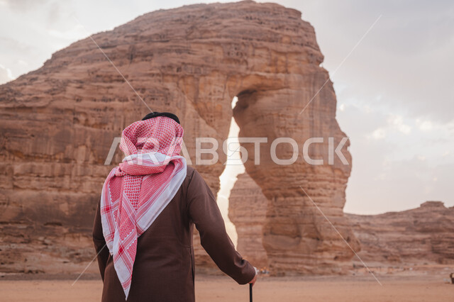 معالم اثرية تاريخية قديمة في وقت النهار، التضاريس في القمم والمرتفعات الجبلية، صورة من الخلف لرجل عربي خليجي سعودي يرتدي الزي التقليدي يستمتع في صحاري المملكة, التكوينات الصخرية في المناطق الصحراوية، اماكن سياحية مشهورة, صخرة الفيل في محافظة العلا في السعودية