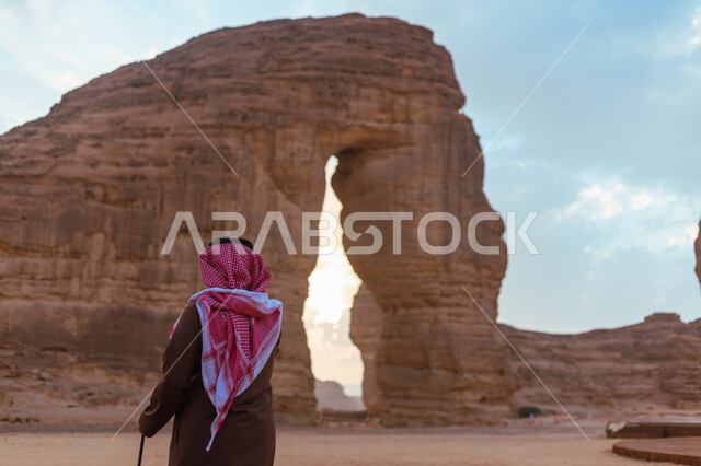 صخرة الفيل في محافظة العلا في السعودية، معالم اثرية تاريخية قديمة في وقت النهار، التضاريس في القمم والمرتفعات الجبلية، صورة من الخلف لرجل عربي خليجي سعودي يرتدي الزي التقليدي يستمتع في صحاري المملكة, التكوينات الصخرية في المناطق الصحراوية، اماكن سياحية مشهورة