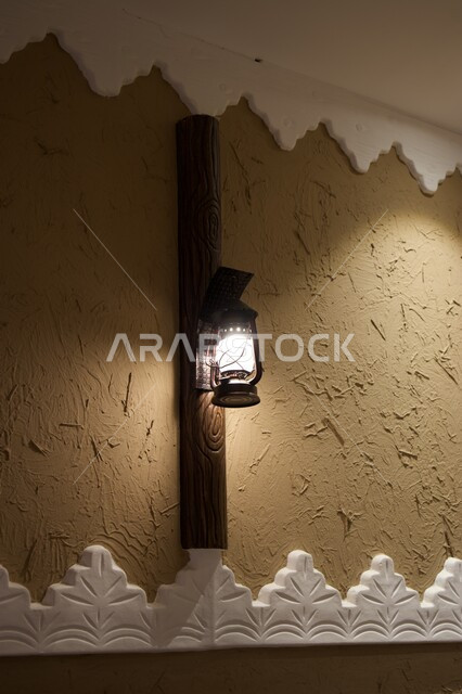 المنشآت المبنية على الطراز الطيني القديم, النقوش والرسومات في البيوت التراثية القديمة, مصباح  معدني مضيء معلق على حائط أثري, التراث والأصالة والعراقة في المملكة العربية السعودية