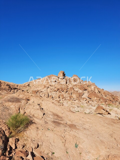  نمو النباتات والاعشاب البرية في المناطق المرتفعة، التكوينات والتشكيلات الصخرية والتضاريس في المملكة العربية السعودية، الاستمتاع بالمناظر الطبيعية في وقت النهار، سلسلة الجبال المجاورة لصخرة سبليت في مدينة تبوك الصحراوية، معالم اثرية تاريخية قديمة سياحية مشهورة