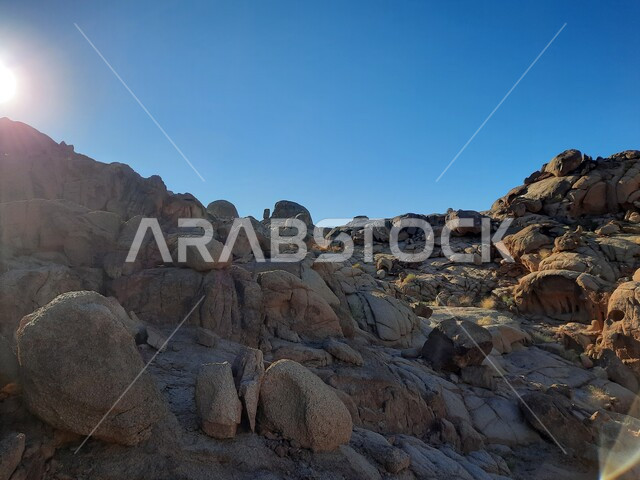 منظر قرص الشمس فوق سلسلة الجبال المجاورة لصخرة سبليت في مدينة تبوك الصحراوية، الاستمتاع بالمناظر الطبيعية في وقت النهار، التضاريس والنحت الصخري في المناطق المرتفعة، التكوينات والتشكيلات الصخرية في السعودية، معالم اثرية تاريخية قديمة سياحية مشهورة