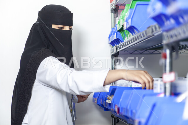 إجراء التجارب العملية, صورة مقربة من الجانب لطبيبة مخبرية عربي خليجية سعودية منقبة ترتدي المعطف الطبي الأبيض تمسك مواد التحليل المخبري, تطور التكنولوجيا الحيوية في المختبرات العلمية, تطوير مهارات البحث الطبي في معامل الكيمياء في المملكة العربية السعودية