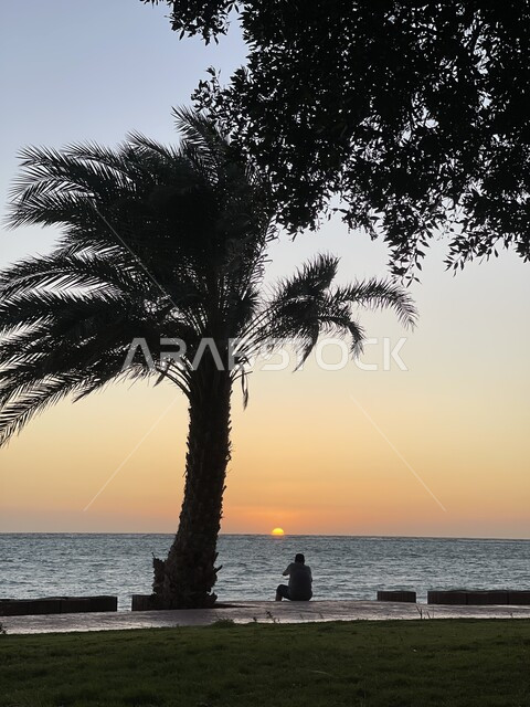  أمواج البحر الهادئة وقت غروب الشمس، صورة من الخلف لرجل عربي خليجي سعودي يتأمل في المناظر الطبيعيه في مدينة ينبع، معالم سياحية ساحلية مشهورة، سيلوليت، خلفية الطبيعه