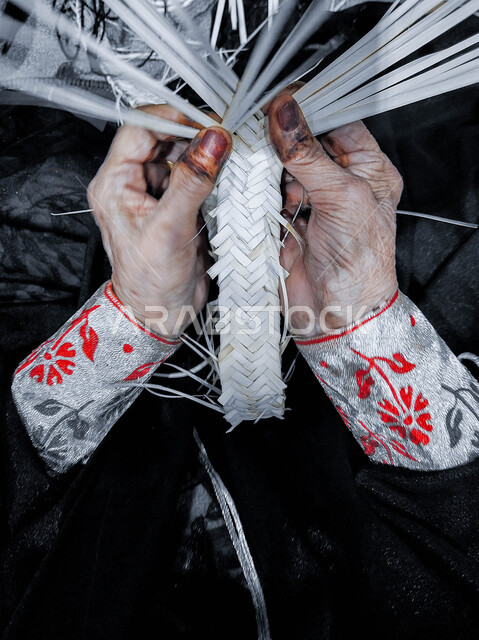 التراث والأصالة في دولة الامارات العربية المتحدة, حرف يدوية تاريخية, أعمال وصناعات قديمة, استخدام أوراق النخيل المجففة في صناعة السلل, منتجات محلية وطنية اماراتية, مهن شعبية تقليدية, صورة مقربة ليد إمرأة عربية خليجية اماراتية تقوم بجدل سعائف الخوص