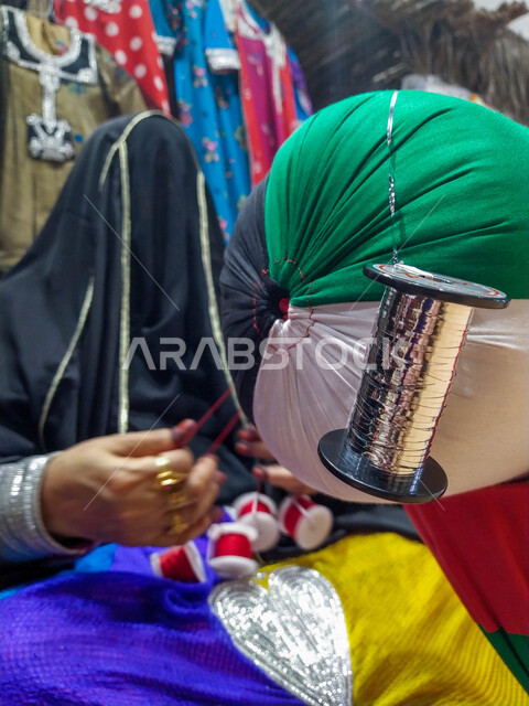 منتجات محلية وطنية اماراتية, مهن وصناعات شعبية, صورة مقربة لإمرأة عربية خليجية اماراتية ترتدي فستان أسود تقليدي تعمل في مجال الحرف اليدوية,الأصالة والعراقة والأشغال التراثية في دولة الامارات