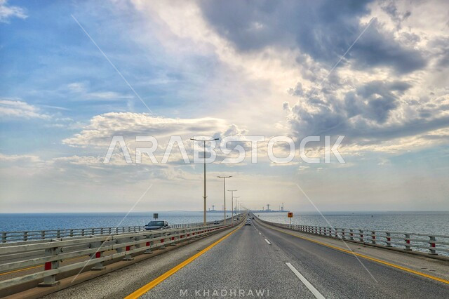منظر السحب البيضاء في سماء السعوديه في وقت النهار، طريق اسفلتي سريع مخصص للسفر بين المدن، جسر معلق ومدعم بالكوابل، التصميم الهندسي المعماري للطرق والشوارع