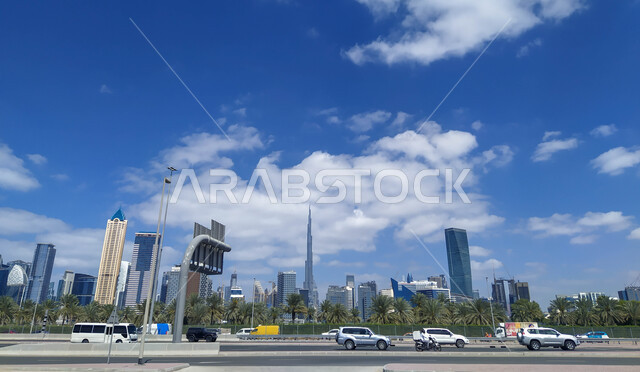 وسائل النقل والمواصلات, التقدم والنمو العمراني المتطور, الحركة المرورية للسيارات في الطرق والشوارع المعبدة في الامارات العربيه المتحدة في وقت النهار, الفن الهندسي المعماري للأبراج وناطحات السحاب في مدينة دبي, خلفية السماء الزرقاء مع الغيوم البيضاء