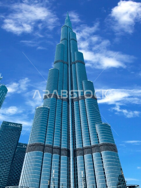 الفن الهندسي المعماري المتقدم للأبراج وناطحات السحاب، العمل على تنمية وتطوير الأبراج والمباني، صورة من الأسفل لبرج خليفة في إمارة دبي، معالم سياحية مشهورة في الإمارات العربية المتحدة، السحب البيضاء في السماء في وقت النهار
