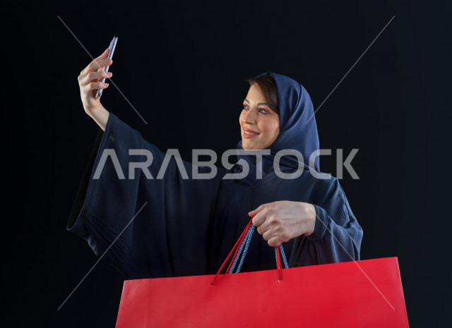 بورتريه مرأه سعودية خليجية تحمل صندوق هدايا كبير ، تستخدم هاتفها المحمول لتصوير صورة سلفي  ، شراء الهدايا ،  الترفيه و التسوق ، يوم التسوق ، الجمعة البيضاء