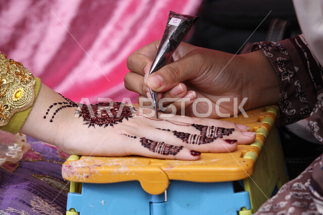 Customs and traditions on happy occasions and weddings, a close-up of the hand of a Saudi Arabian Gulf woman drawing and engraving by a girl using red henna, adornment, beautification and attention to the external appearance, traditional folk professions for women, decorations and handmade arts from natural materials.