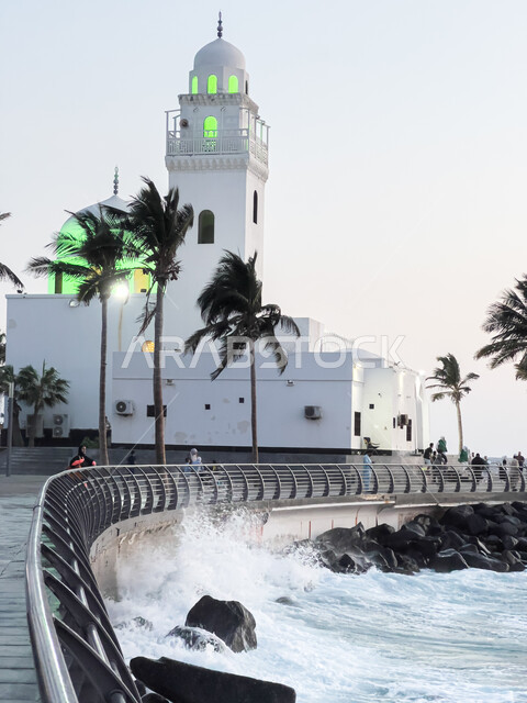 أشجار النخيل الخضراء على الواجهة البحرية، معالم سياحية مشهورة في السعودية، اماكن اسلاميه دينية مقدسة ،أمواج البحر الهادئة على الشاطئ في النهار، الفن الهندسي المعماري لمسجد الجزيرة على كورنيش مدينة جدة