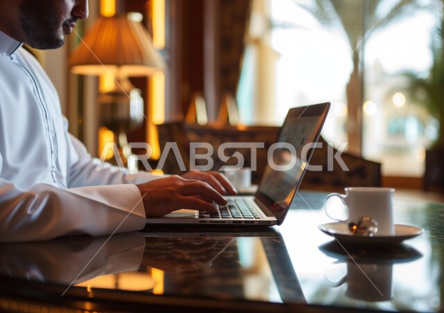 Conducting agreements and conversations via the Internet, gestures of focus, contemplation, and precision, integrating technology and technology into work, a close-up photo of a Saudi Gulf Arab man using a laptop, business management and organization, office professions and jobs