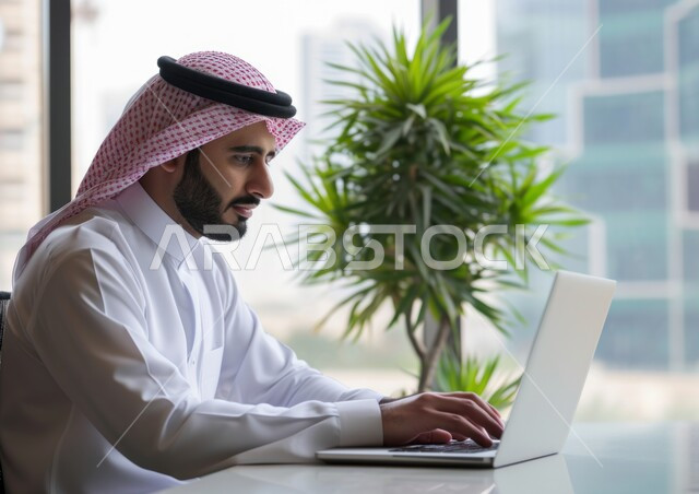 تحقيق الأهداف والاستراتيجيات, إيماءات التركيز والتمعن والدقة في العمل, مهن ووظائف مكتبية, صورة مقربة لرجل عربي خليجي سعودي يرتدي الشماغ والثوب التقليدي يقوم باستخدام الحاسب المحمول, إدارة وتنظيم الأعمال ضمن مقر الشركة