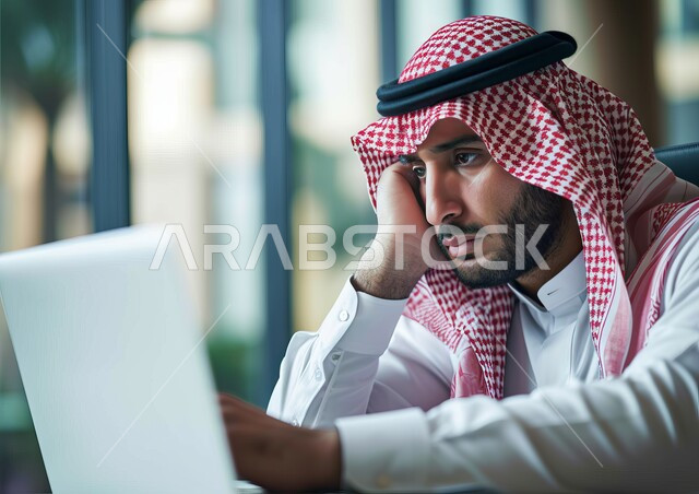 إيماءات التأمل والتفكير في حل المشكلات, مفهوم ضغط العمل, مهن ووظائف مكتبية, صورة مقربة لرجل عربي خليجي سعودي يرتدي الشماغ والثوب التقليدي يقوم باستخدام الحاسب المحمول,  إدارة وتنظيم الأعمال ضمن مقر الشركة