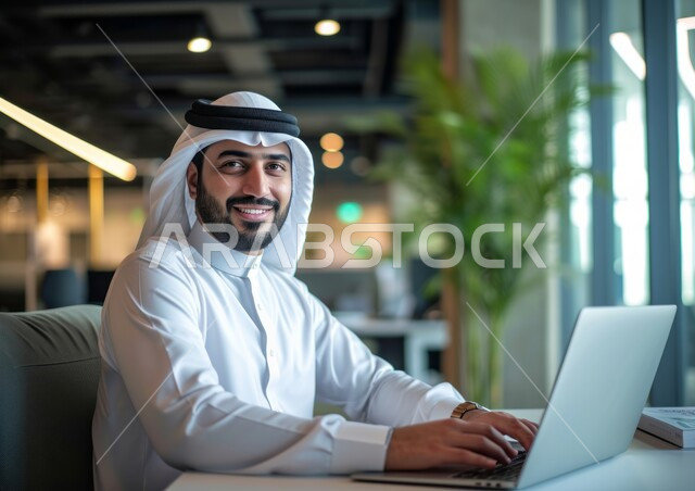 دمج التقنية والتكنولوجيا مع الحياة العملية, بيئة العمل المريحة في الشركات السعودية, إيماءات السرور والفرح, صورة مقربة لرجل عربي خليجي سعودي مبتسم يرتدي الشماغ والثوب التقليدي ينظر إلى الكاميرا يقوم باستخدام الحاسب المحمول, إدارة وتنظيم الأعمال ضمن مقر الشركة