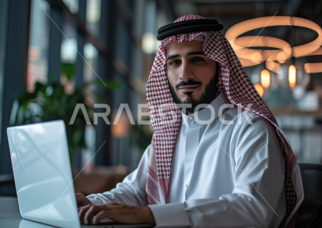 Completing office tasks using a laptop, comfortable work environment in Saudi companies, close-up photo of a smiling Saudi Gulf Arab man wearing a shemagh and traditional thobe looking at the camera with self-confidence gestures, integrating technology and technology with practical life