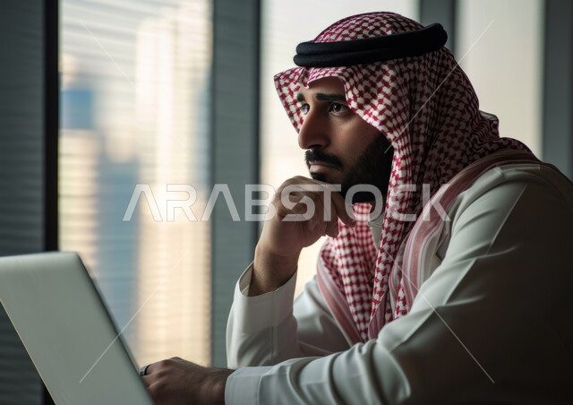 إيماءات التأمل والتفكير في حل المشكلات, مهن ووظائف مكتبية, صورة مقربة لرجل عربي خليجي سعودي يرتدي الشماغ والثوب التقليدي يضع يده تحت رأسه يقوم باستخدام الحاسب المحمول, بيئة العمل المريحة في الشركات السعودية, إدارة وتنظيم الأعمال ضمن مقر الشركة