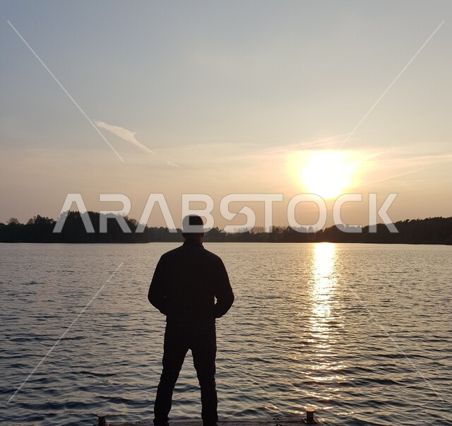 الاسترخاء والاستجمام والاستمتاع بالهدوء, صورة ظلية من الخلف لشاب عربي خليجي سعودي يقف أمام البحر يتأمل المناظر الطبيعية وقت غروب الشمس, أماكن سياحية في المملكة العربية السعودية