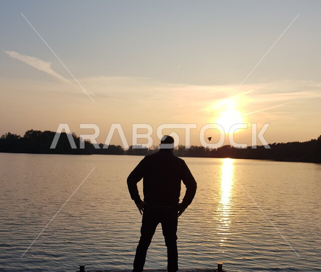 الاسترخاء والاستجمام والاستمتاع بالهدوء, صورة ظلية من الخلف لشاب عربي خليجي سعودي يقف أمام البحر يتأمل المناظر الطبيعية وقت غروب الشمس, أماكن سياحية في المملكة العربية السعودية