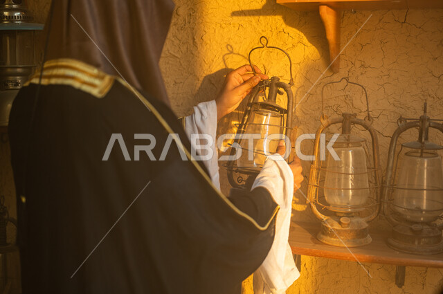 الفخر والاعتزاز بالهوية السعودية، المناسبات والأعياد الوطنية، صورة مقربة من الخلف لرجل عربي خليجي سعودي يرتدي العقال والبشت التقليدي يمسك بيده فانوس معدني، ذكرى تأسيس الدولة السعودية الاولى 22 فبراير، توارث حب التراث القديم من الأجداد، يوم بدينا 1727 م