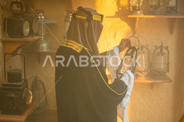 ذكرى تأسيس الدولة السعودية الاولى 22 فبراير، يوم بدينا 1727 م، المناسبات والأعياد الوطنية، صورة مقربة من الخلف لرجل عربي خليجي سعودي يرتدي العقال والبشت التقليدي يمسك بيده فانوس معدني، الاعتزاز والفخر بالهوية السعودية، توارث حب التراث القديم من الأجداد