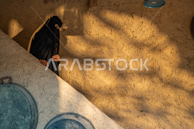 The day of the founding of the first Saudi state, February 22, a Saudi Gulf Arab woman wearing a burqa and a black abaya in an old-style mud heritage house, the anniversary of the Day of Debt 1727 AD, pride and pride in belonging to the homeland, wearing popular costumes on national occasions and holidays.