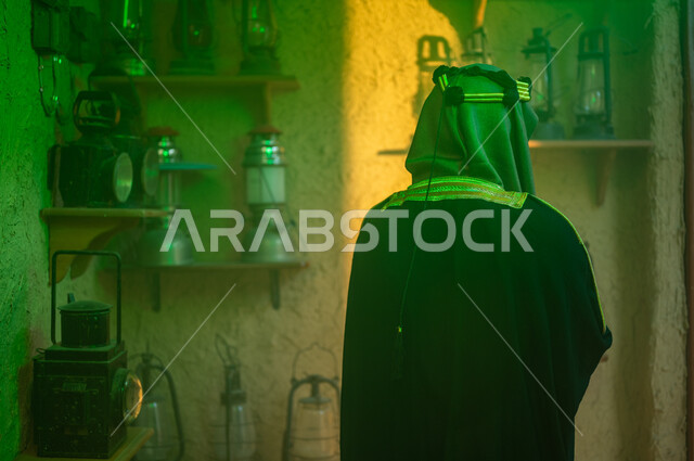 الفخر والاعتزاز بالهوية السعودية، توارث حب التراث القديم من الأجداد، ذكرى تأسيس الدولة السعودية الاولى 22 فبراير، يوم بدينا 1727 م، المناسبات والأعياد الوطنية، صورة مقربة من الخلف لرجل عربي خليجي سعودي يرتدي البشت والزي التقليدي ينظر إلى الفوانيس المعدنية
