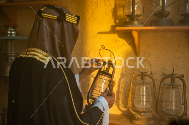 الاعتزاز والفخر بالهوية السعودية، توارث حب التراث القديم من الأجداد، ذكرى تأسيس الدولة السعودية الاولى 22 فبراير، يوم بدينا 1727 م، المناسبات والأعياد الوطنية، صورة مقربة من الخلف لرجل عربي خليجي سعودي يرتدي البشت والزي التقليدي يمسك بيده فانوس معدني