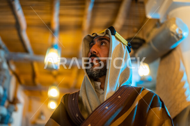 اظهار التفاني والولاء للبلاد ،ارتداء الأزياء الشعبيه للمناسبات والأعياد الوطنية، ذكرى تأسيس الدولة السعودية الاولى 22 فبراير، يوم بدينا 1727 م، صورة مقربة لرجل عربي خليجي سعودي يرتدي الزي التقليدي والعقال في أحد البيوت الطينية التراثيه القديمة ينظر الى شيء ما