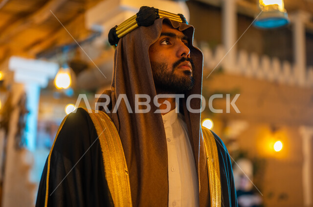 النظر الى شيء ما بإيماءات الحزم والقوة والثقة, الأحياء والمنازل التراثية الشعبية الطينية القديمة, يوم بدينا 1727 م، الأعياد والمناسبات الوطنية في السعودية, صورة مقربة لرجل عربي خليجي سعودي يرتدي البشت والعقال في ذكرى تأسيس الدولة السعودية الأولى في 22 فبراير