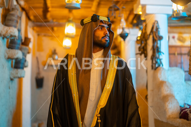 Anniversary of the founding of the first Saudi state on February 22, standing with gestures of confidence, firmness and strength, old mud folk heritage neighborhoods and houses, Badina Day 1727 AD, national holidays and events in Saudi Arabia, a close-up of a Saudi Gulf Arab man wearing a bisht and aqal looking at something