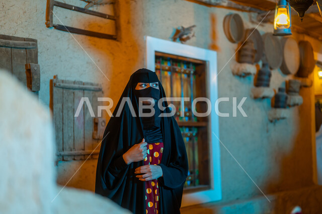 التباهي والاعتزاز بالهوية السعودية ،ذكرى تاسيس الدولة السعودية الاولى 22 فبراير، ارتداء الأزياء الشعبيه للمناسبات والأعياد الوطنية ، يوم بدينا 1727 م، امرأة عربية خليجية سعودية ترتدي البرقع والعباءة السوداء تقف في أحد البيوت التراثيه المبنية على الطراز القديم