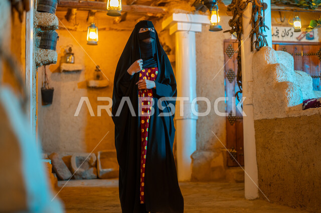 الاعتزاز والفخر بالهوية السعودية ،ذكرى تاسيس الدولة السعودية الاولى 22 فبراير، ارتداء الأزياء الشعبيه للمناسبات والأعياد الوطنية ،امرأة عربية خليجية سعودية ترتدي البرقع والعباءة السوداء تقف في أحد البيوت التراثيه المبنية على الطراز القديم،  يوم بدينا 1727 م