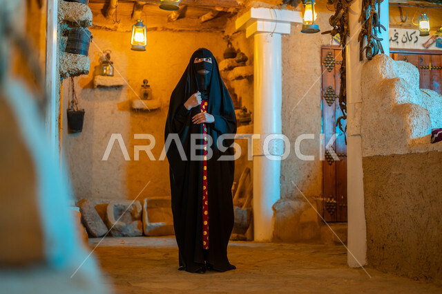 ذكرى تاسيس الدولة السعودية الاولى 22 فبراير، الفخر والاعتزاز بالهوية السعودية ،ارتداء الأزياء الشعبيه للمناسبات والأعياد الوطنية ،امرأة عربية خليجية سعودية ترتدي البرقع والعباءة السوداء تقف في أحد البيوت التراثيه المبنية على الطراز القديم،  يوم بدينا 1727 م