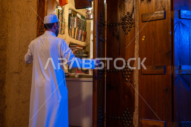 تنمية ودعم الذخيرة اللغوية والعلمية, صورة من الخلف لرجل عربي خليجي سعودي يرتدي الثوب التقليدي والقبعه البيضاء يقوم بفتح باب المكتبة الخشبي الأثري التراثي, ذكرى تأسيس الدولة السعودية الأولى 22 فبراير، يوم بدينا 1727 م، المكاتب التاريخيه المبنية على الطراز القديم