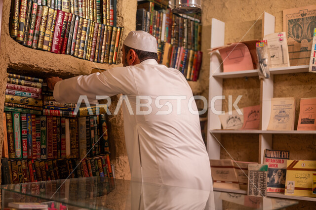 يوم بدينا 1727 م ،دعم وتنمية الذخيرة العلمية, مفهوم الثقافة والتعلم الذاتي, صورة من الخلف لرجل عربي خليجي سعودي يرتدي الثوب التقليدي والقبعه البيضاء يقوم بترتيب الكتب على الرفوف في المكتبة المبنية على الطراز القديم, ذكرى تأسيس الدولة السعودية الأولى 22 فبراير