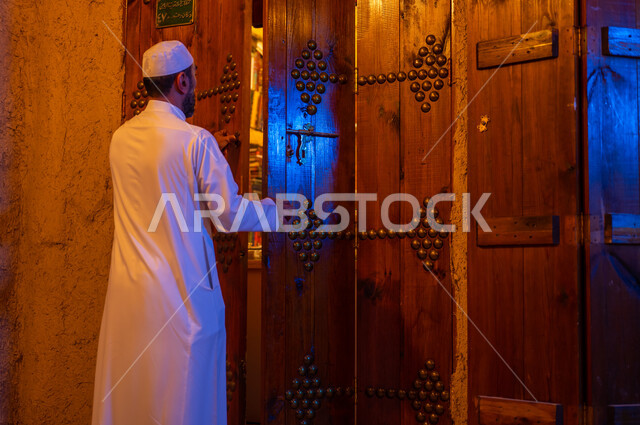 المكاتب التاريخيه المبنية على الطراز القديم، دعم وتنمية الذخيرة اللغوية والعلمية, صورة من الخلف لرجل عربي خليجي سعودي يرتدي الثوب التقليدي والقبعه البيضاء يقوم بفتح باب خشبي اثري تراثي, ذكرى تأسيس الدولة السعودية الأولى 22 فبراير، يوم بدينا 1727 م