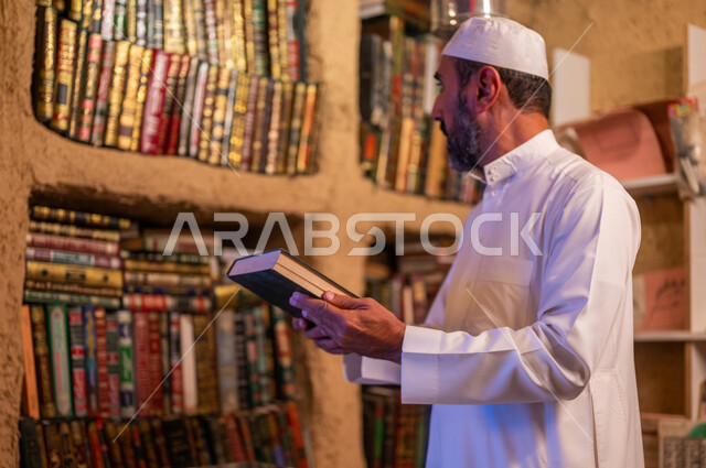 استعارة الكتب من المكاتب التاريخيه المبنية على الطراز القديم، دعم وتنمية الذخيرة اللغوية والعلمية, رجل عربي خليجي سعودي يرتدي الثوب التقليدي والقبعه البيضاء يقوم باقتناء كتاب من المكتبة, ذكرى تأسيس الدولة السعودية الأولى 22 فبراير، يوم بدينا 1727 م