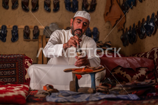 الحرف و المهن اليدوية التقليدية القديمة, يوم بدينا 1727 م، صناعات و أعمال شعبية, ذكرى تأسيس الدولة السعودية الأولى 22 فبراير ،متجر اصلاح الأحذية، اسكافي عربي خليجي سعودي يرتدي الثوب التقليدي والقبعه البيضاء يقوم بصناعة الحذاء وتصليحه بالأدوات المناسبة