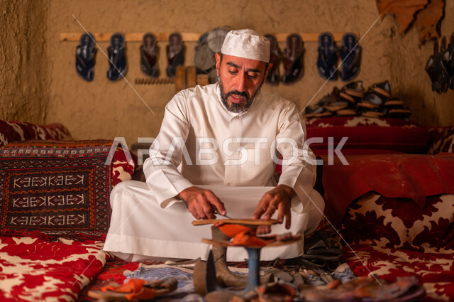 أعمال وصناعات تقليدية شعبية, الحرف والمهن اليدوية في السعودية, مفهوم إحياء التراث الشعبي، متجر اصلاح الأحذية، اسكافي عربي خليجي سعودي يرتدي الثوب التقليدي والقبعه البيضاء يقوم بصناعة الحذاء وتصليحه، ذكرى تأسيس الدولة السعودية الأولى 22 فبراير، يوم بدينا 1727 م