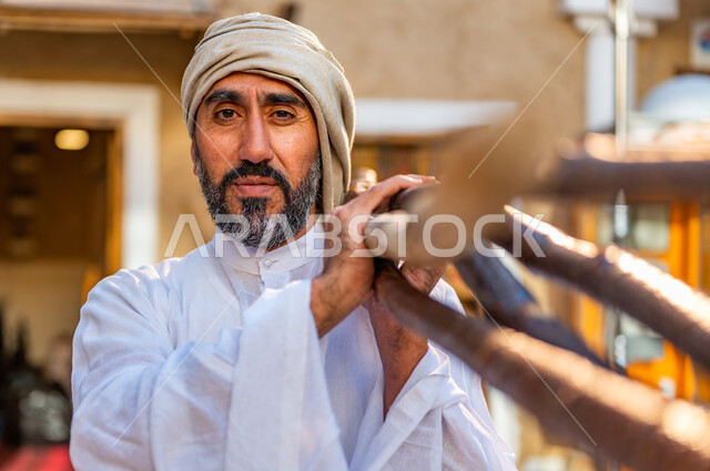 يوم بدينا 1727 م، ذكرى تأسيس الدولة السعودية الأولى 22 فبراير، تجميع الحطب في موسم الشتاء, صورة مقربة لفلاح عربي خليجي سعودي يرتدي الزي الشعبي يحمل مجموعه من أعواد الخشب الثقيلة على كتفه داخل البيوت التراثية، الحياة التقليدية البدوية، وسائل التدفئة القديمة