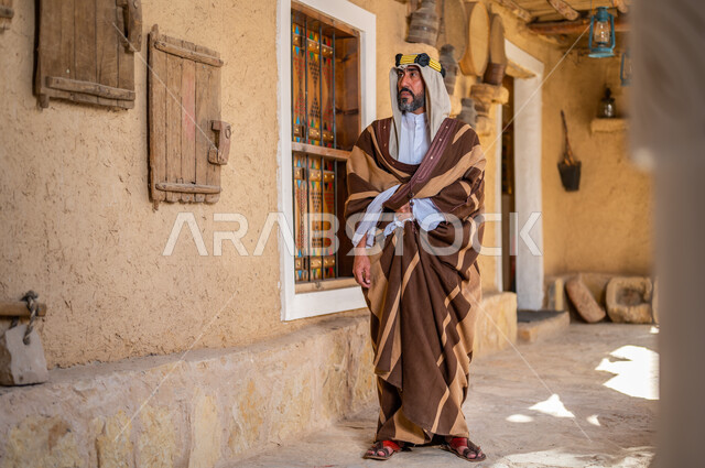ارتداء الأزياء الشعبية في ذكرى تأسيس الدولة السعودية الاولى 22 فبراير، يوم بدينا 1727 م، الفخر والاعتزاز بالهوية السعودية، المناسبات والأعياد الوطنية، رجل عربي خليجي سعودي يرتدي العقال والبشت التقليدي في منزل طيني قديم
