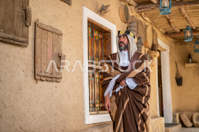 ارتداء الأزياء الشعبية في ذكرى تأسيس الدولة السعودية الاولى 22 فبراير، يوم بدينا 1727 م، الفخر والاعتزاز بالهوية السعودية، المناسبات والأعياد الوطنية، رجل عربي خليجي سعودي يرتدي العقال والبشت التقليدي في منزل طيني قديم